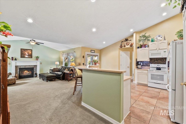 kitchen with a breakfast bar, white appliances, light colored carpet, vaulted ceiling, and white cabinetry