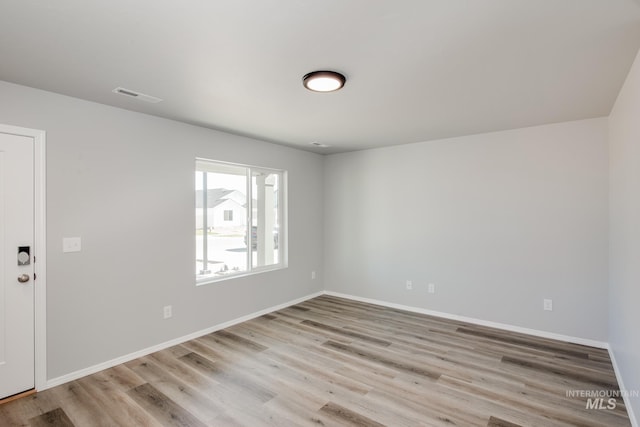 spare room featuring light wood-type flooring, visible vents, and baseboards