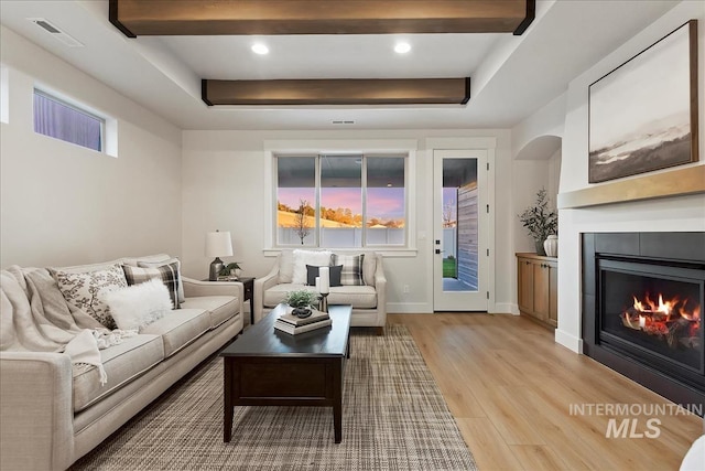 living room with beam ceiling, a tray ceiling, plenty of natural light, and light wood-type flooring