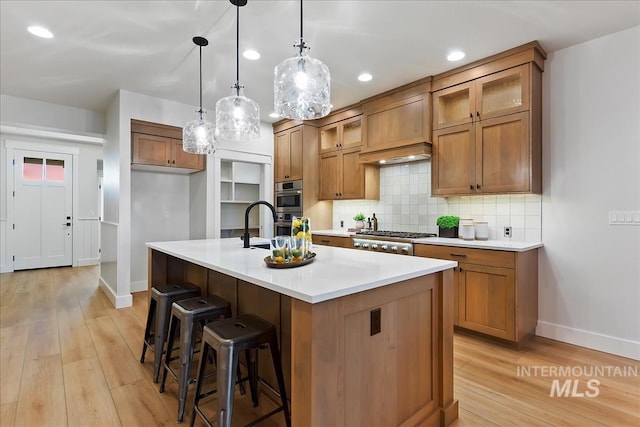 kitchen with a center island with sink, light hardwood / wood-style flooring, pendant lighting, stainless steel appliances, and decorative backsplash