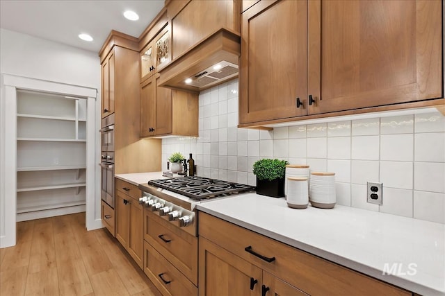 kitchen with premium range hood, stainless steel gas cooktop, backsplash, and light hardwood / wood-style flooring