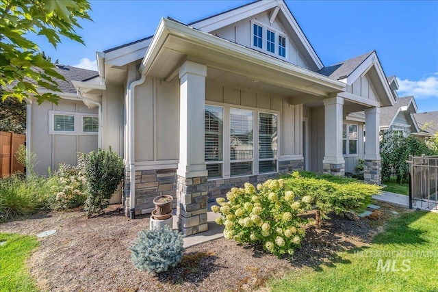 craftsman-style house with stone siding, roof with shingles, board and batten siding, and fence