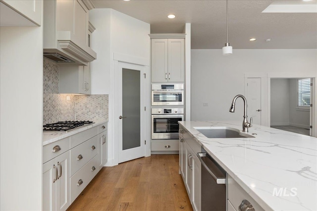 kitchen with light wood-type flooring, pendant lighting, custom range hood, sink, and stainless steel appliances