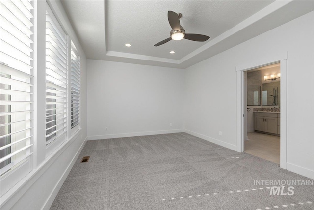 interior space with a tray ceiling, carpet floors, ceiling fan, and ensuite bath