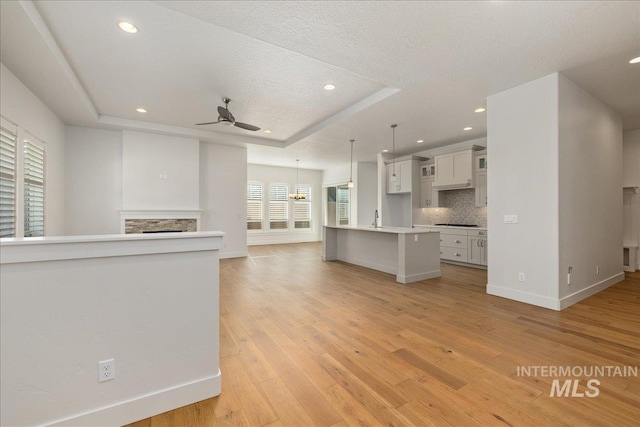 interior space featuring light wood-type flooring, tasteful backsplash, a multi sided fireplace, a raised ceiling, and ceiling fan