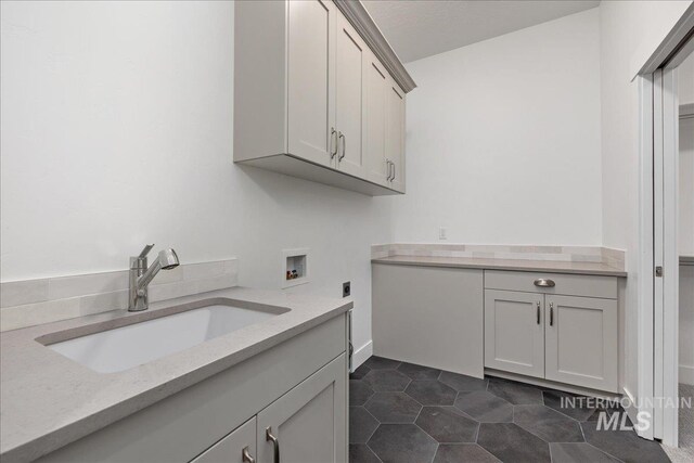 laundry room featuring sink, electric dryer hookup, dark tile patterned flooring, washer hookup, and cabinets