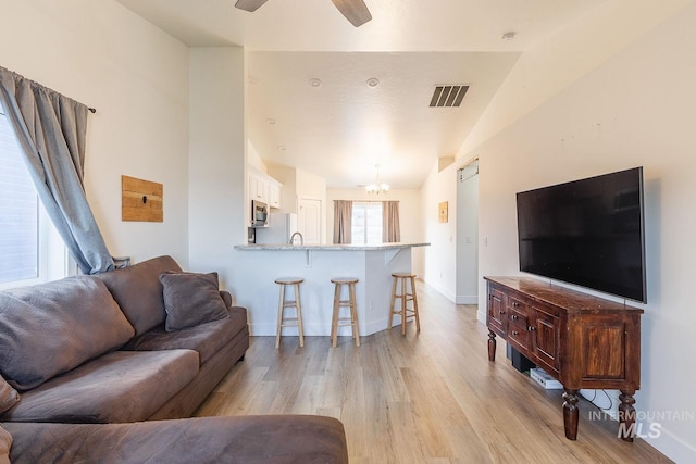 living room featuring lofted ceiling, ceiling fan with notable chandelier, and light hardwood / wood-style flooring