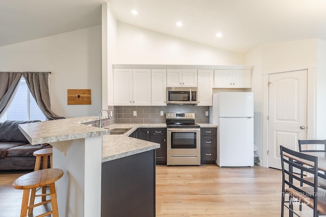 kitchen with vaulted ceiling, stainless steel appliances, white cabinets, and sink