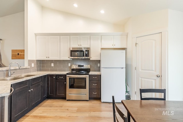 kitchen featuring tasteful backsplash, vaulted ceiling, sink, white cabinetry, and appliances with stainless steel finishes