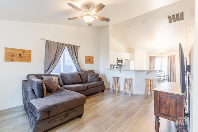 living room with ceiling fan with notable chandelier, lofted ceiling, and light wood-type flooring