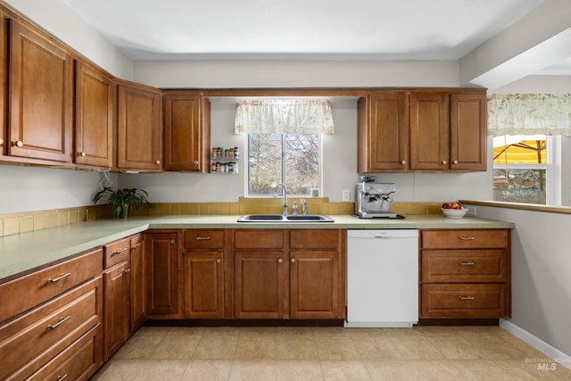kitchen featuring a sink, light countertops, white dishwasher, and brown cabinetry