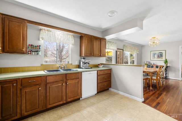 kitchen featuring light countertops, plenty of natural light, brown cabinets, a sink, and white dishwasher