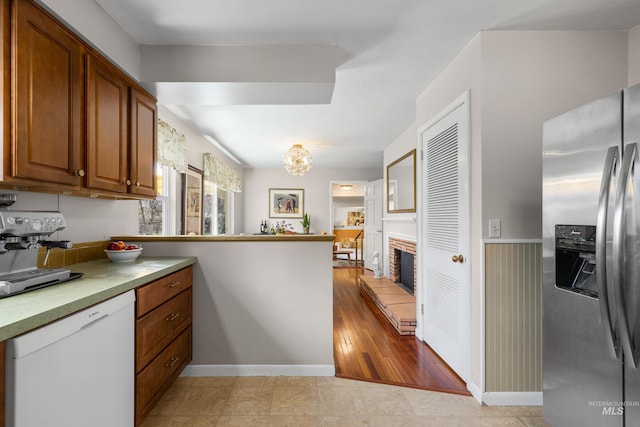 kitchen featuring stainless steel refrigerator with ice dispenser, a peninsula, white dishwasher, brown cabinets, and wainscoting