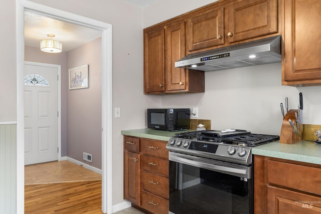 kitchen featuring black microwave, brown cabinetry, under cabinet range hood, stainless steel gas range oven, and visible vents
