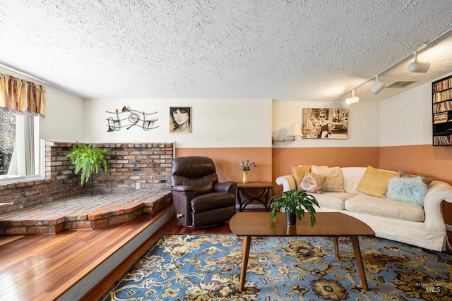 living area featuring rail lighting, visible vents, a textured ceiling, and wood finished floors