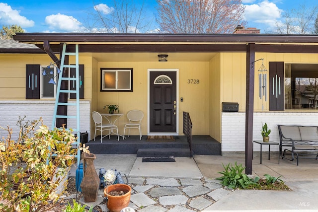property entrance featuring brick siding, a chimney, and a porch