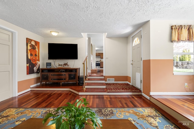 foyer entrance featuring wood finished floors, a textured ceiling, baseboards, and visible vents