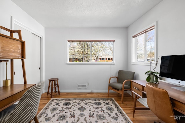 office area featuring baseboards, visible vents, a textured ceiling, and wood finished floors
