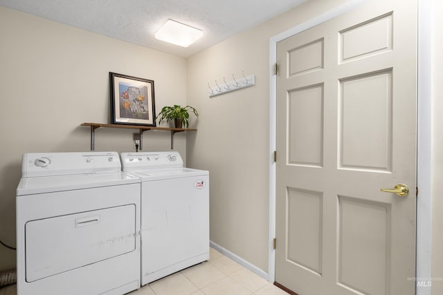 washroom featuring baseboards, a textured ceiling, light tile patterned flooring, washer and dryer, and laundry area