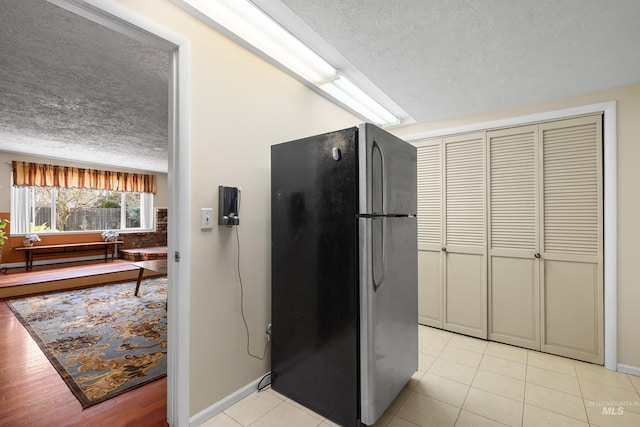 kitchen with freestanding refrigerator, light tile patterned floors, baseboards, and a textured ceiling