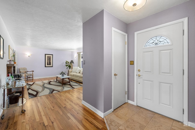 foyer featuring light wood finished floors, baseboards, and a textured ceiling