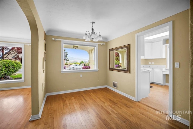 3205 W Crescent Rim Dr, Boise, ID 83706 - unfurnished dining area with a chandelier, light wood-style floors, baseboards, and arched walkways