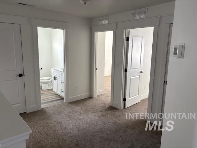 unfurnished bedroom featuring ensuite bath and light colored carpet