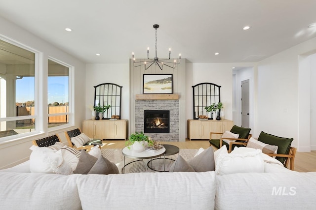 living room featuring light wood-type flooring, an inviting chandelier, and a brick fireplace