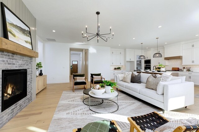 living room featuring a brick fireplace, sink, a chandelier, and light wood-type flooring