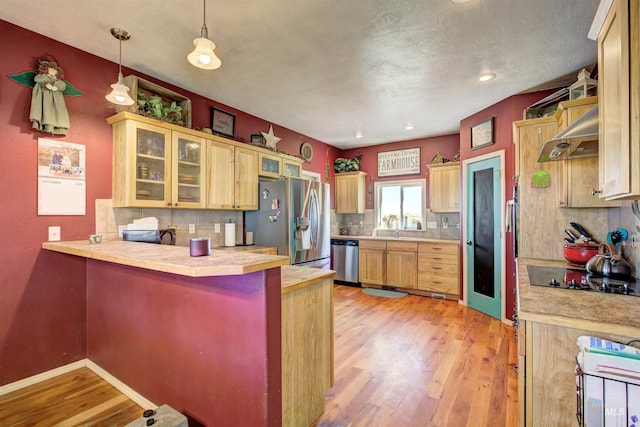 28284 Tudie Ln, Parma, ID 83660 - kitchen featuring tasteful backsplash, range hood, light wood-type flooring, a peninsula, and appliances with stainless steel finishes