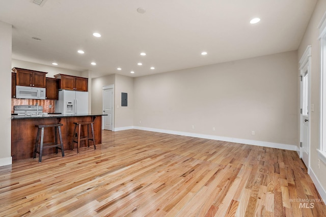 kitchen featuring electric panel, white appliances, a kitchen bar, and light wood finished floors