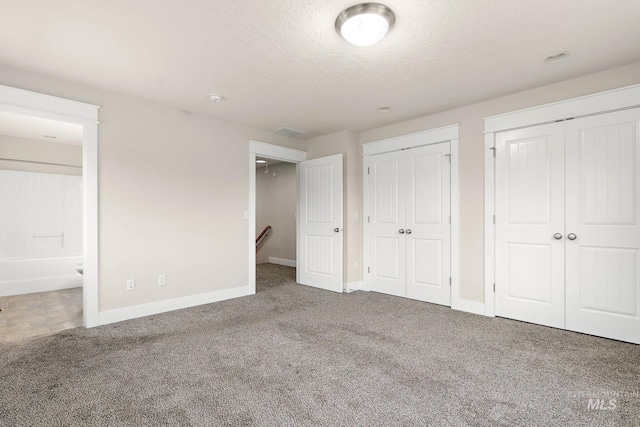 unfurnished bedroom with a textured ceiling, baseboards, carpet flooring, and multiple closets