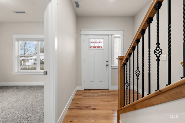 entryway with light wood finished floors, stairway, visible vents, and baseboards