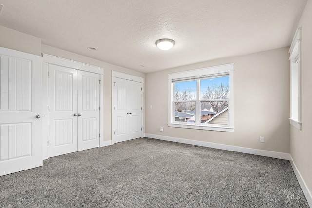 unfurnished bedroom with carpet, a textured ceiling, baseboards, and multiple closets