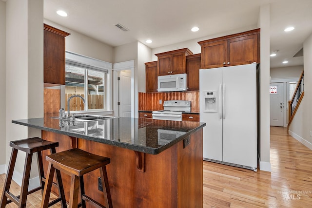 kitchen featuring light wood-style flooring, a peninsula, white appliances, a sink, and dark stone countertops