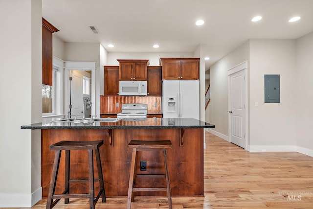 kitchen with visible vents, a sink, dark stone countertops, white appliances, and a peninsula