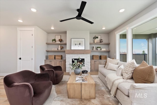 living room with light wood finished floors, a stone fireplace, recessed lighting, and ceiling fan