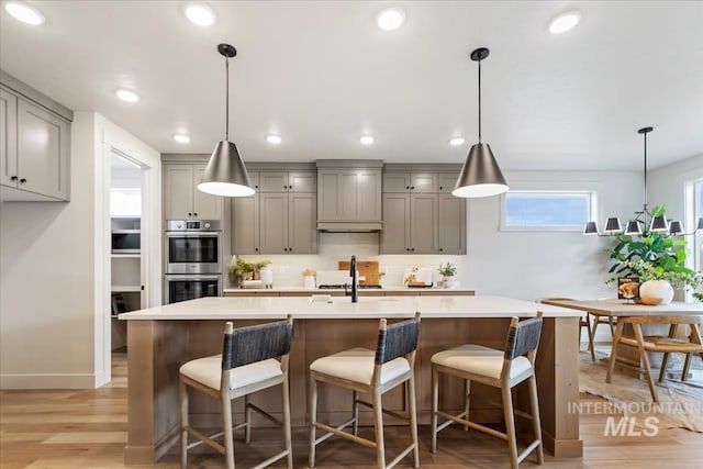 kitchen with gray cabinetry, light wood-style flooring, a sink, double oven, and light countertops