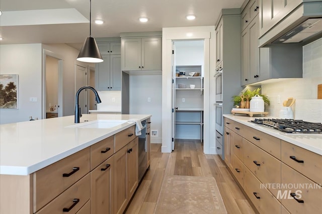 kitchen featuring custom exhaust hood, stainless steel appliances, a sink, light countertops, and light wood-type flooring