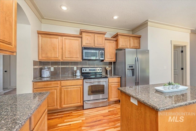 2895 E Shadowwolf Dr, Eagle, ID 83616 - kitchen with stainless steel appliances, light wood-style floors, backsplash, dark stone countertops, and arched walkways