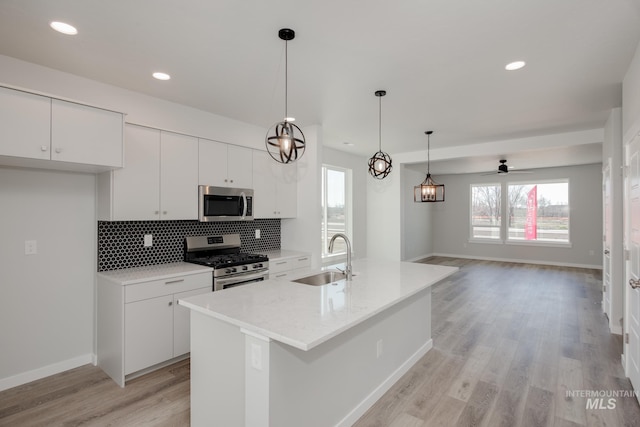 kitchen featuring an island with sink, stainless steel appliances, white cabinetry, pendant lighting, and a sink