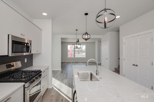 kitchen featuring stainless steel appliances, pendant lighting, white cabinetry, and a sink