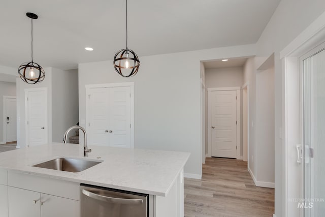 kitchen with hanging light fixtures, stainless steel dishwasher, a kitchen island with sink, white cabinets, and a sink