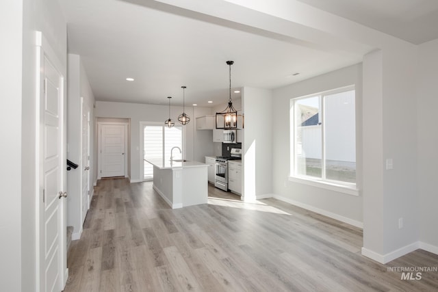 kitchen featuring stainless steel appliances, a sink, light countertops, an island with sink, and pendant lighting