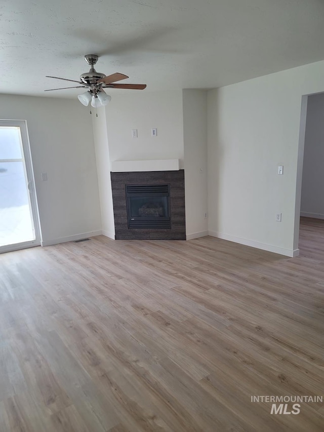 unfurnished living room with a glass covered fireplace, wood finished floors, ceiling fan, and baseboards
