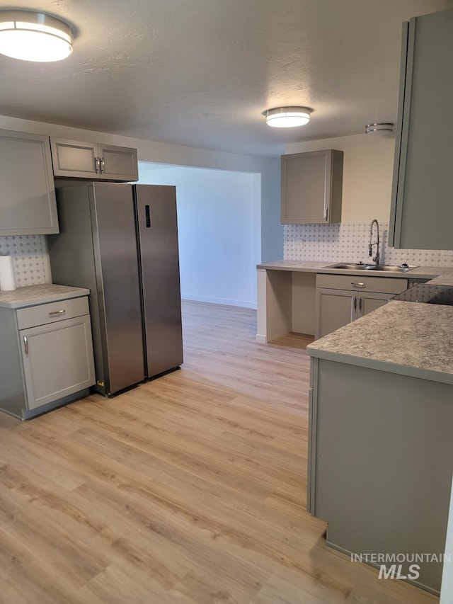 kitchen with gray cabinetry, a sink, freestanding refrigerator, backsplash, and light wood finished floors