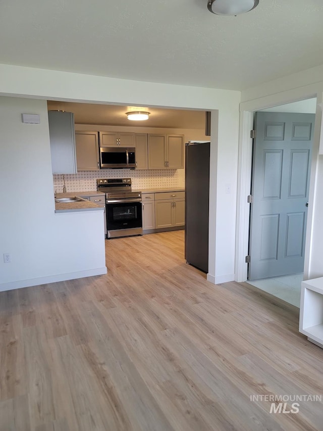 kitchen with appliances with stainless steel finishes, backsplash, light wood-style flooring, light countertops, and baseboards