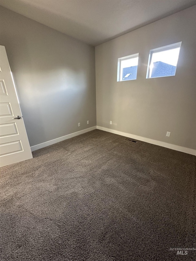 unfurnished room with baseboards and dark colored carpet