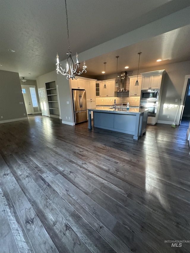 kitchen featuring wall chimney range hood, stainless steel appliances, baseboards, a chandelier, and dark wood-style floors