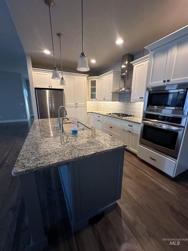 kitchen featuring appliances with stainless steel finishes, wall chimney exhaust hood, a sink, dark wood-style flooring, and decorative backsplash